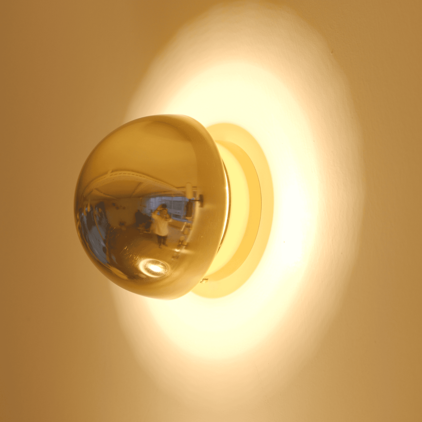 A polished brass wall sconce with a rounded form reflects light for elegant ambient lighting.