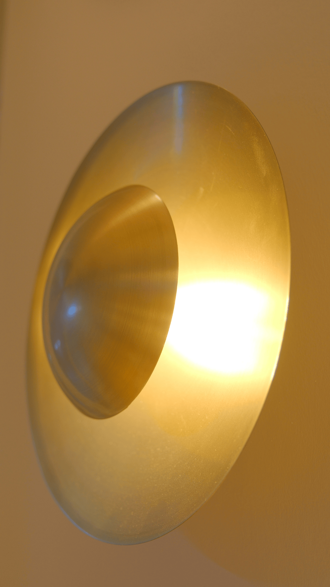 Sculptural convex brass wall sconce radiating warm ambient light.