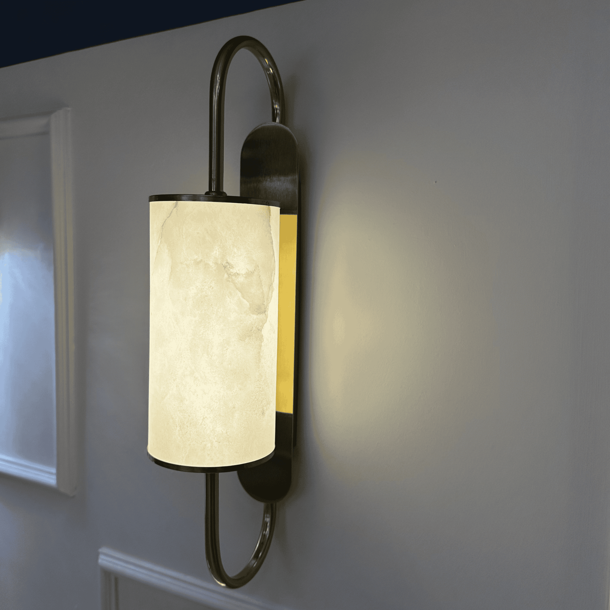 Angled close-up of illuminated brass wall sconce with alabaster shade and side lighting glow.