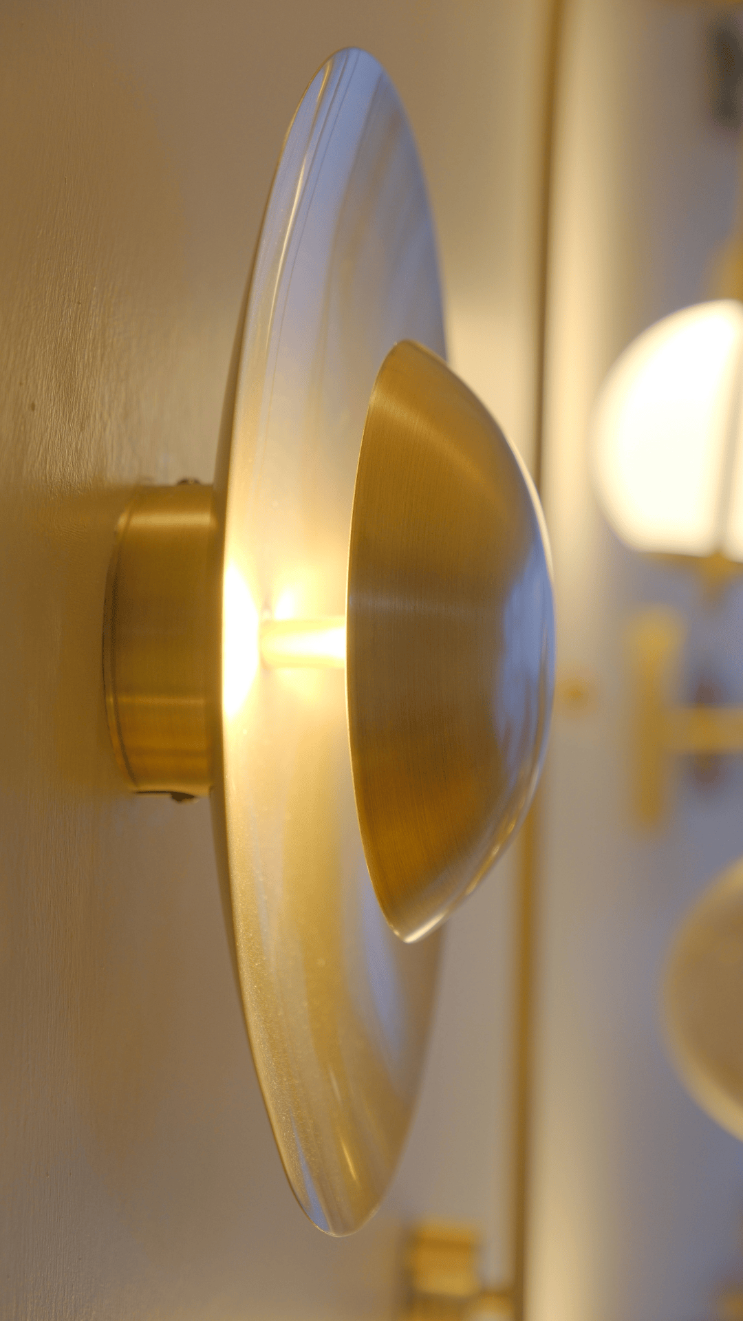 Side view of brushed brass wall sconce with layered disk design emitting warm light.