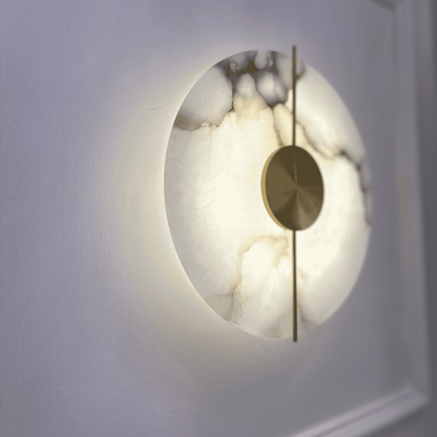 Close side view of a marble sconce with brass accents glowing warmly.