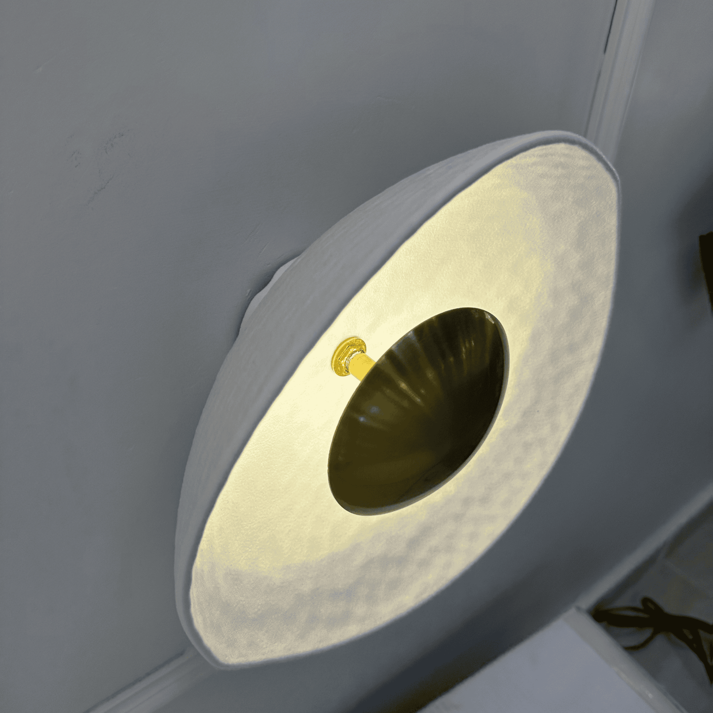 Side view of a deco wall sconce with brass core and translucent white hammered shade mounted on a wall.