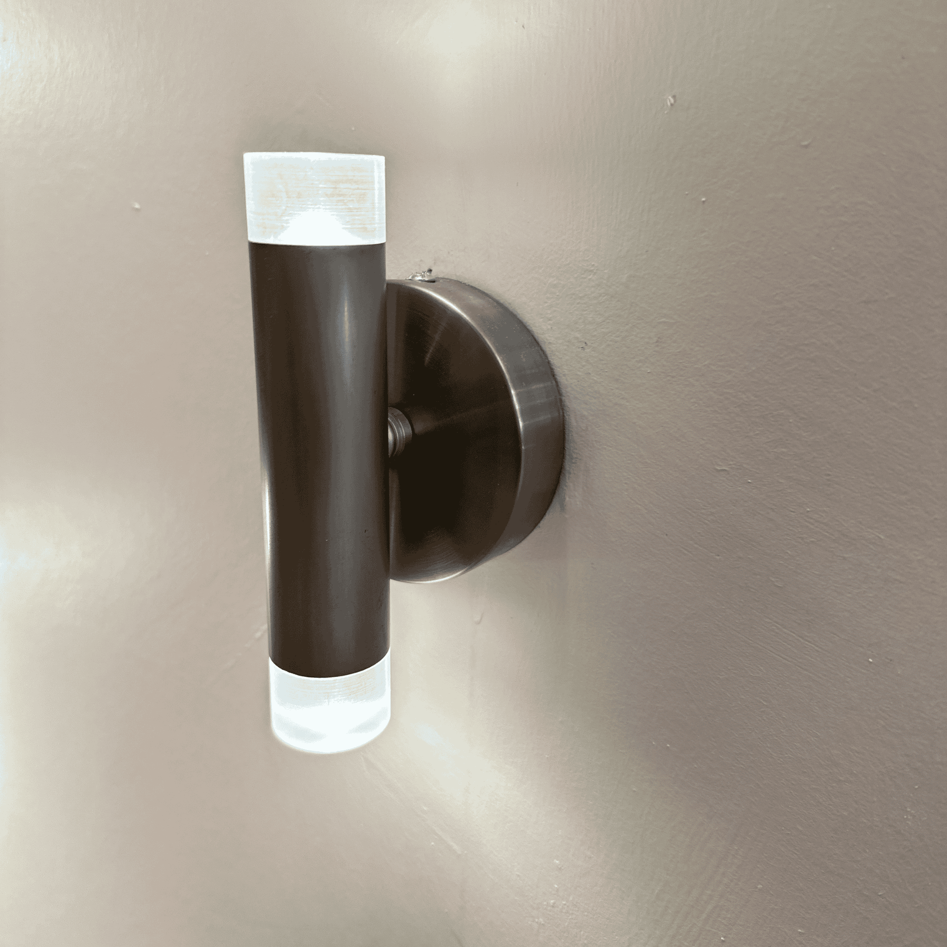 Side view of a black cylindrical LED wall sconce mounted on a wall, glowing from top and bottom for ambient lighting.