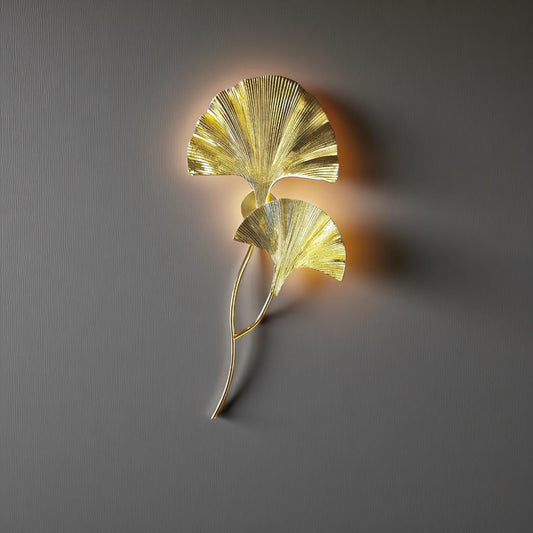 Tall sculptural wall sconce in a gold finish, mounted on a neutral interior wall