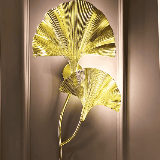 Close-up of Solace gold wall sconce with two ginkgo leaf shapes on a paneled wall