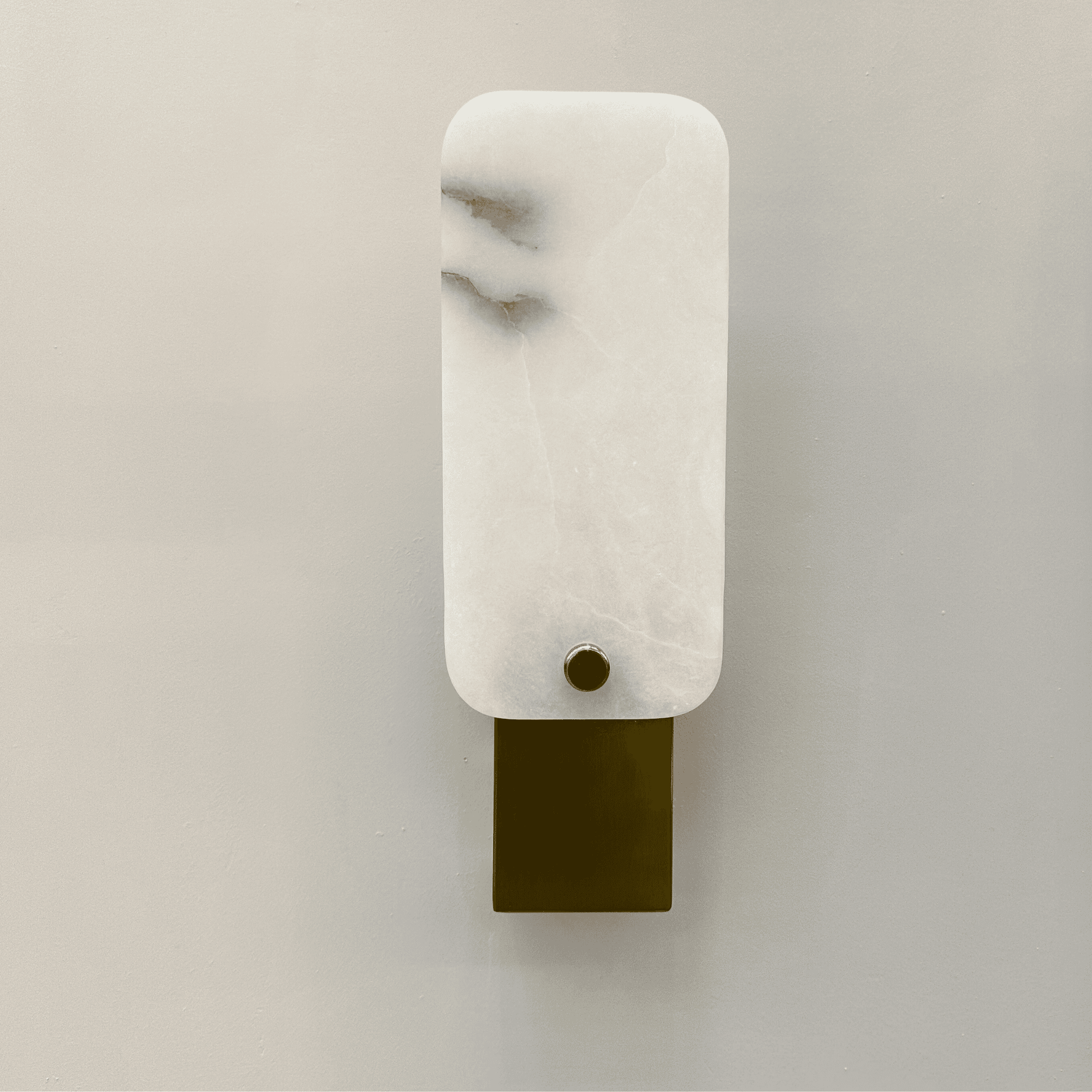 Square marble wall lamp with white stone shade and brushed brass base mounted on a neutral wall.