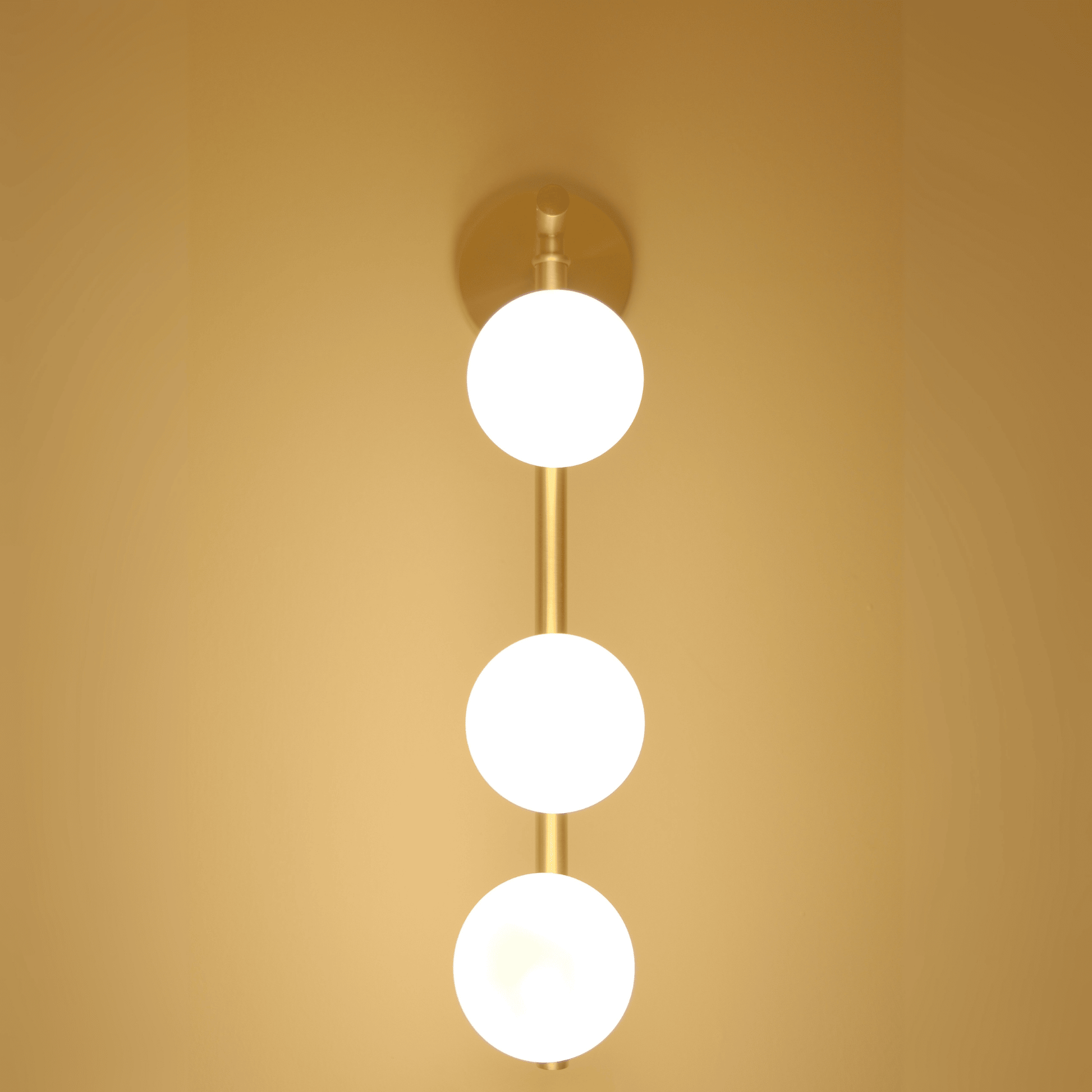 Brass wall light with three illuminated frosted glass globes viewed straight on.
