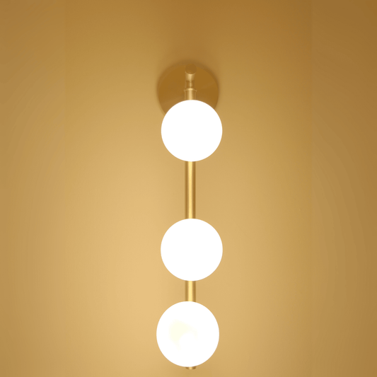 Brass wall light with three illuminated frosted glass globes viewed straight on.