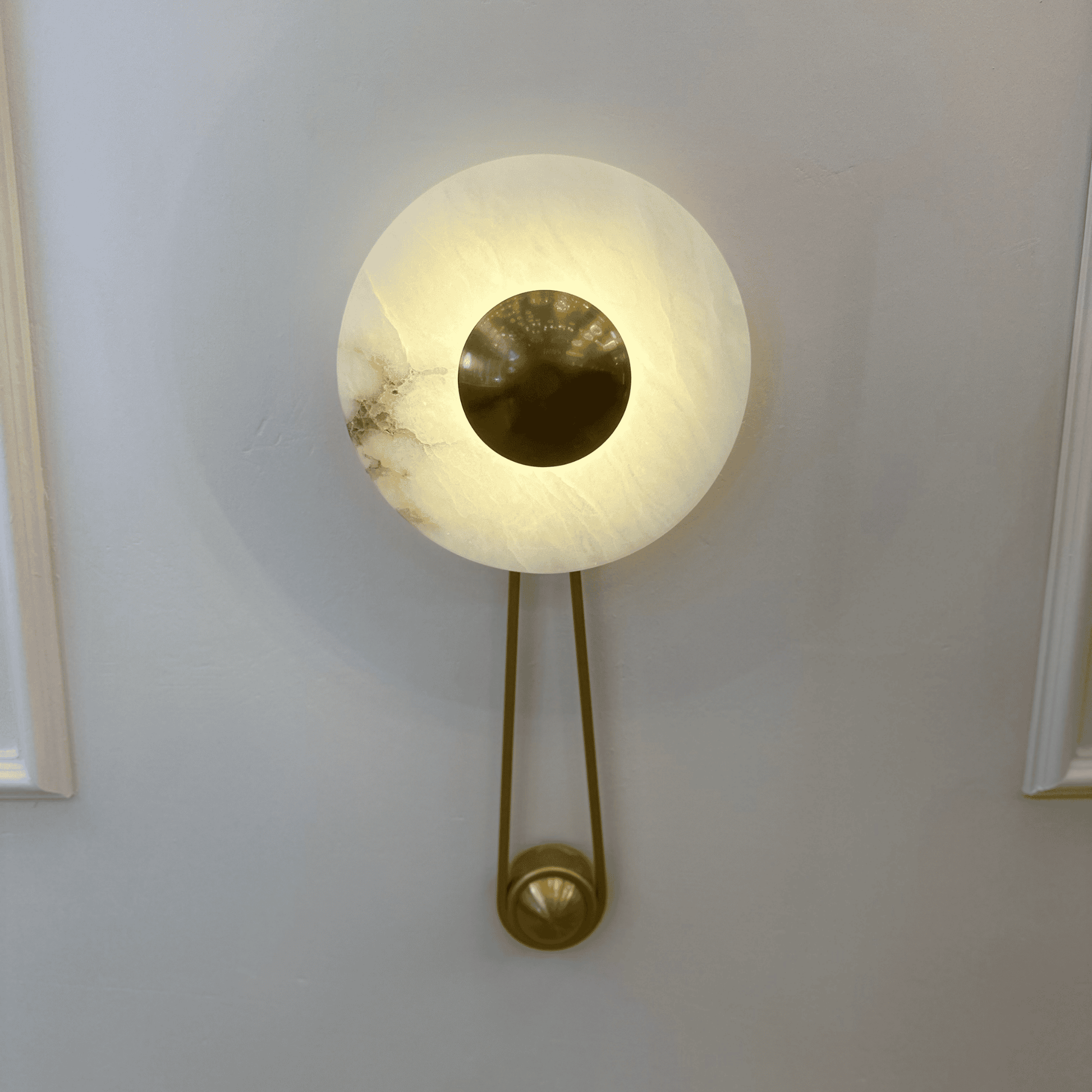 Front view of alabaster wall sconce with central round brass disc on a paneled interior wall.
