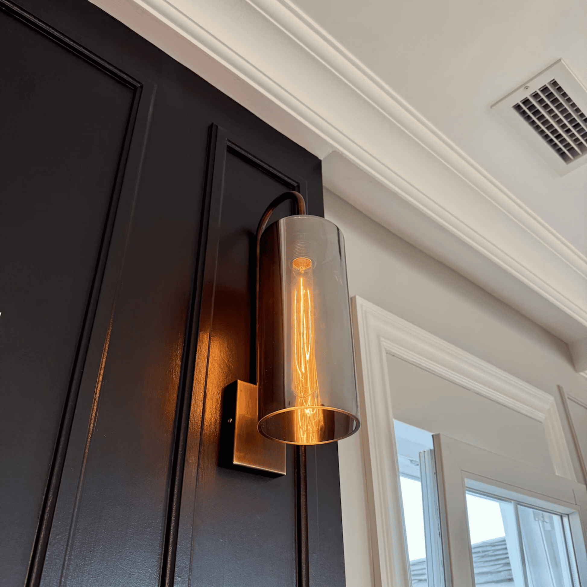 Tall blown glass wall sconce with Edison bulb and antique backplate casting warm light.