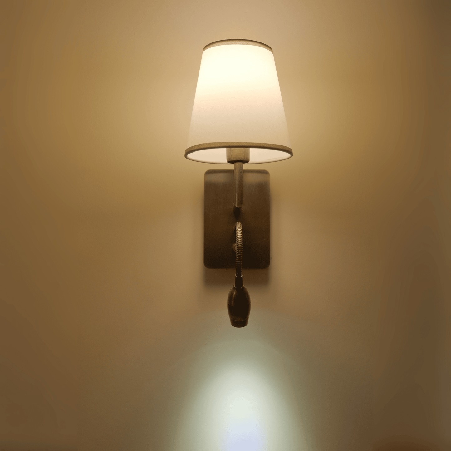 Wall sconce with metallic finish and flexible light casting a downward glow.