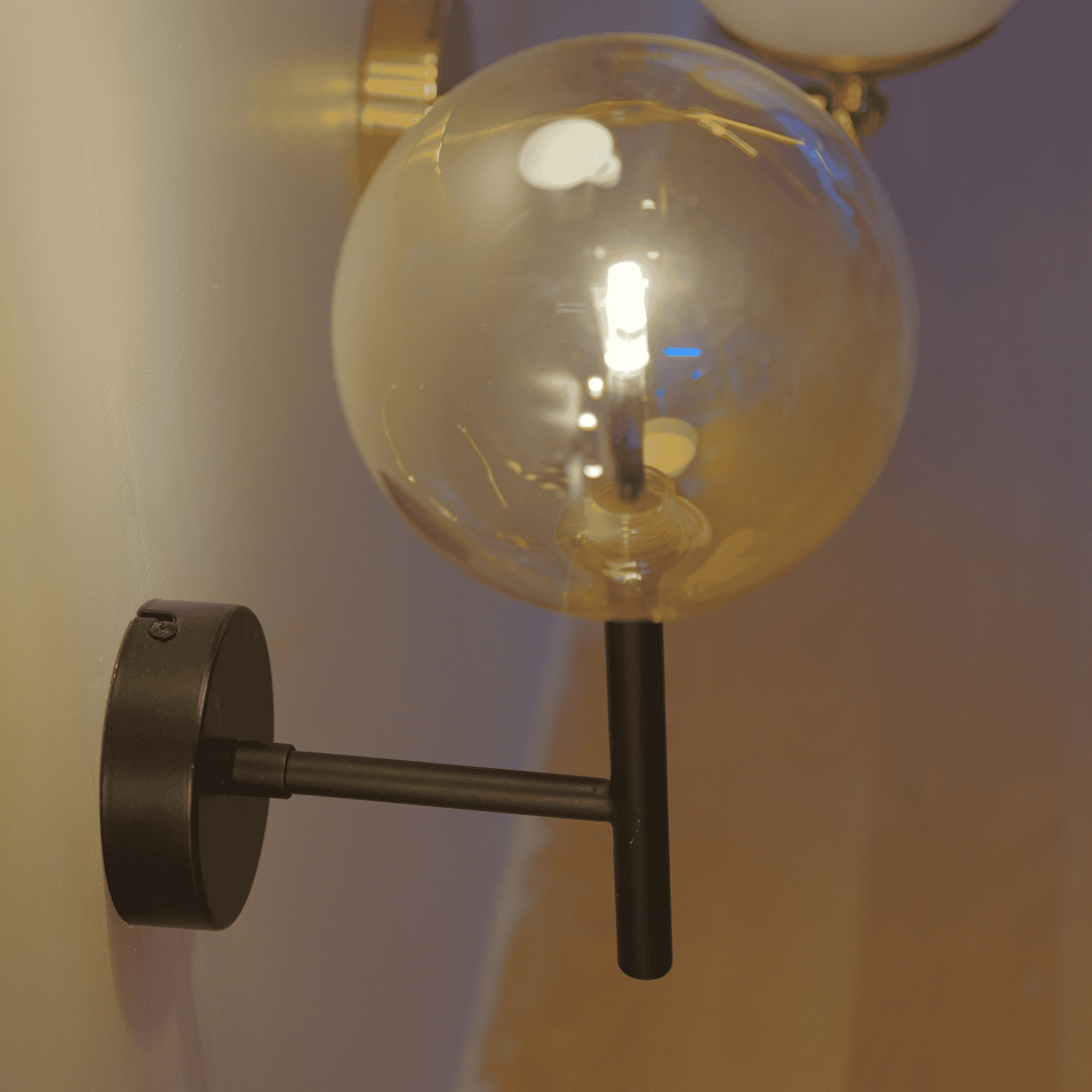 Vertical black sconce with clear glass globe and warm LED light.