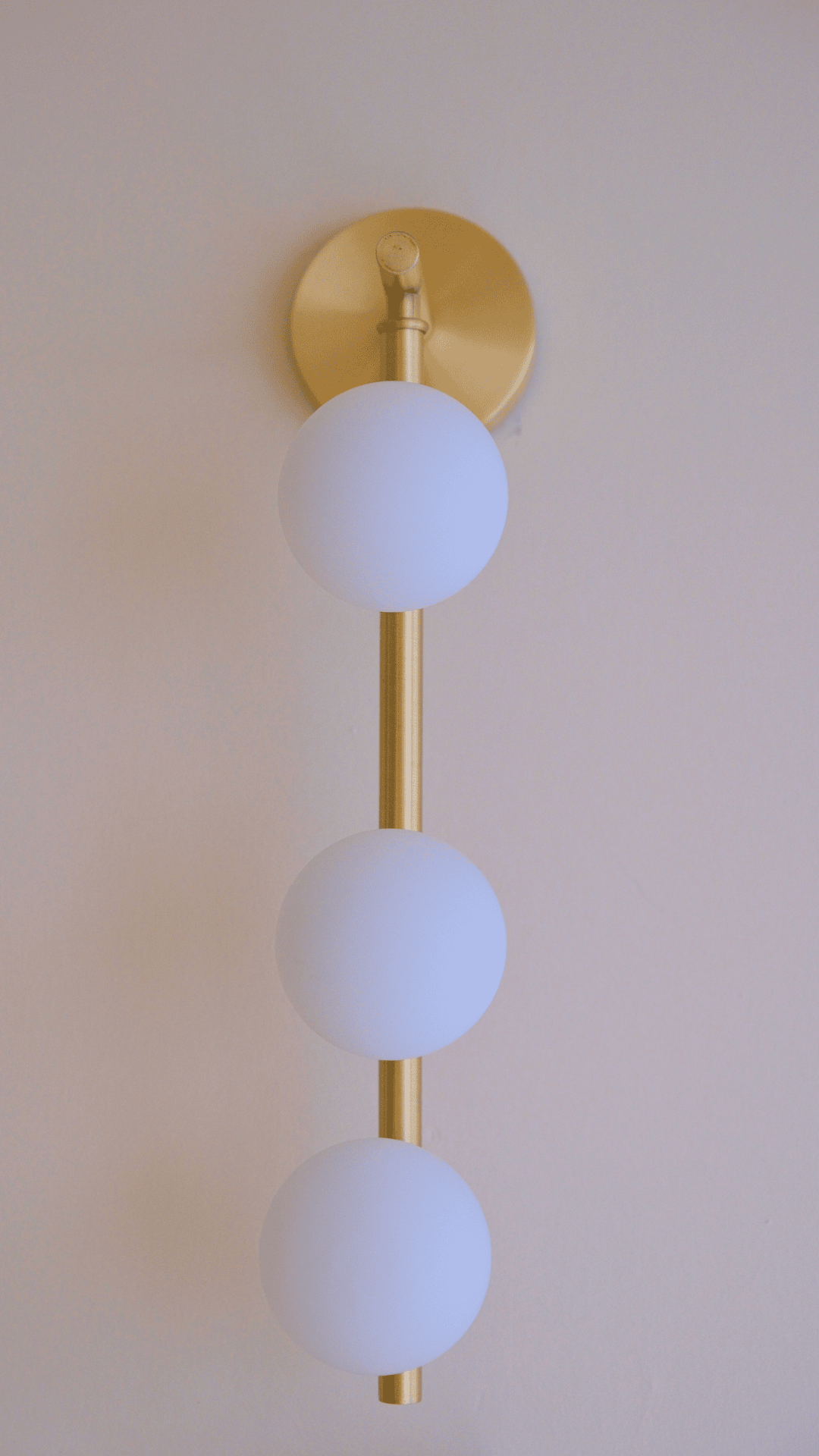 Vertical brass wall sconce featuring three evenly spaced frosted globe lights for modern interiors.