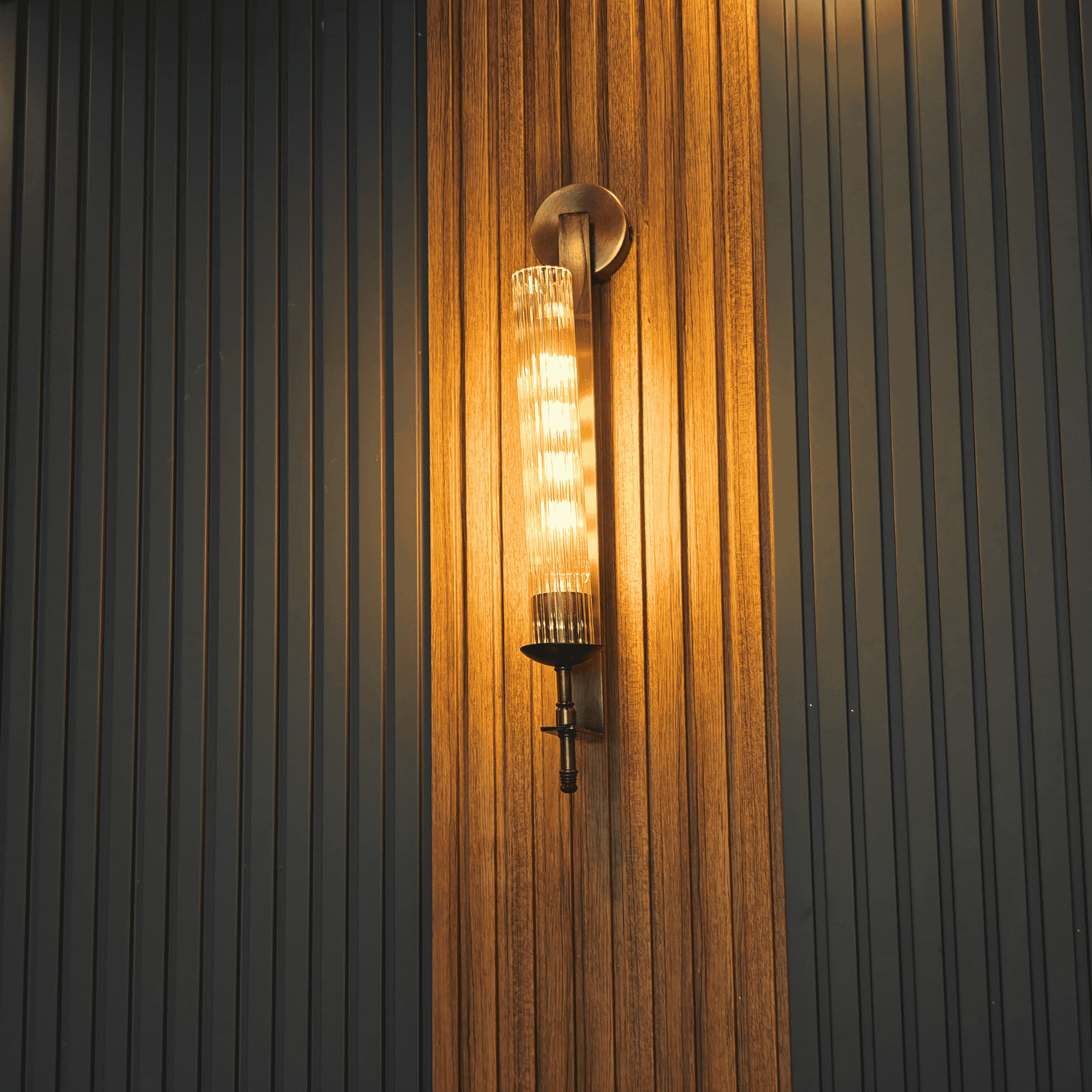 Ribbed glass wall sconce casting warm light on vertical wood slat feature wall