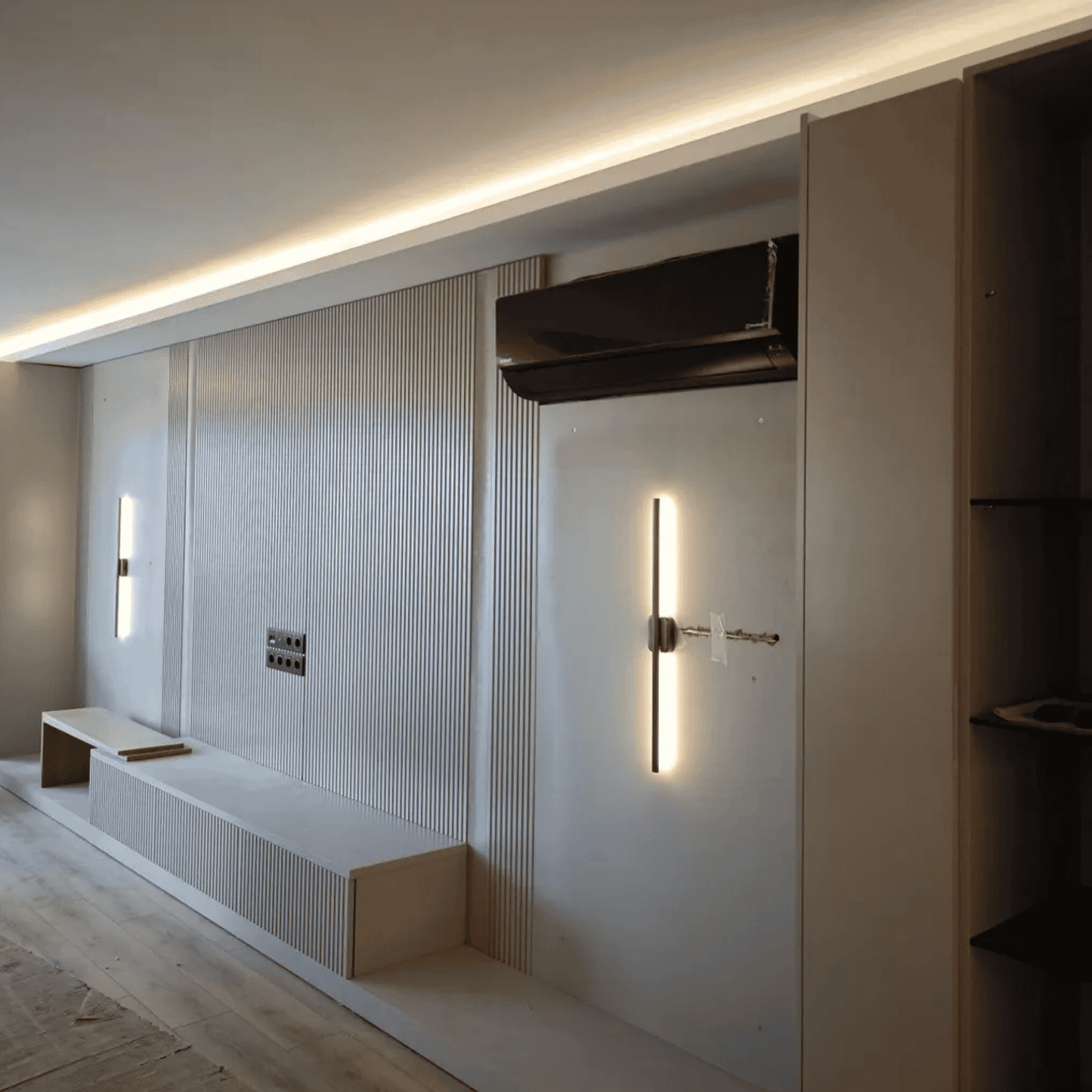 Vertical wall sconce with soft glow installed in a modern room with recessed ceiling lights and paneled walls under construction.