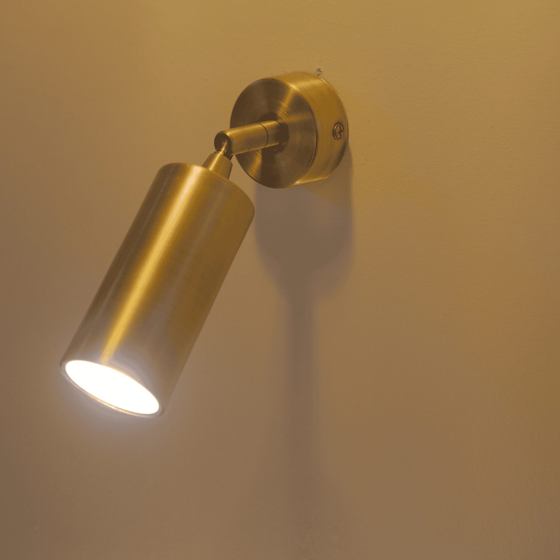 Brass cylinder wall sconce in a lighting showroom casting a bright focused beam.