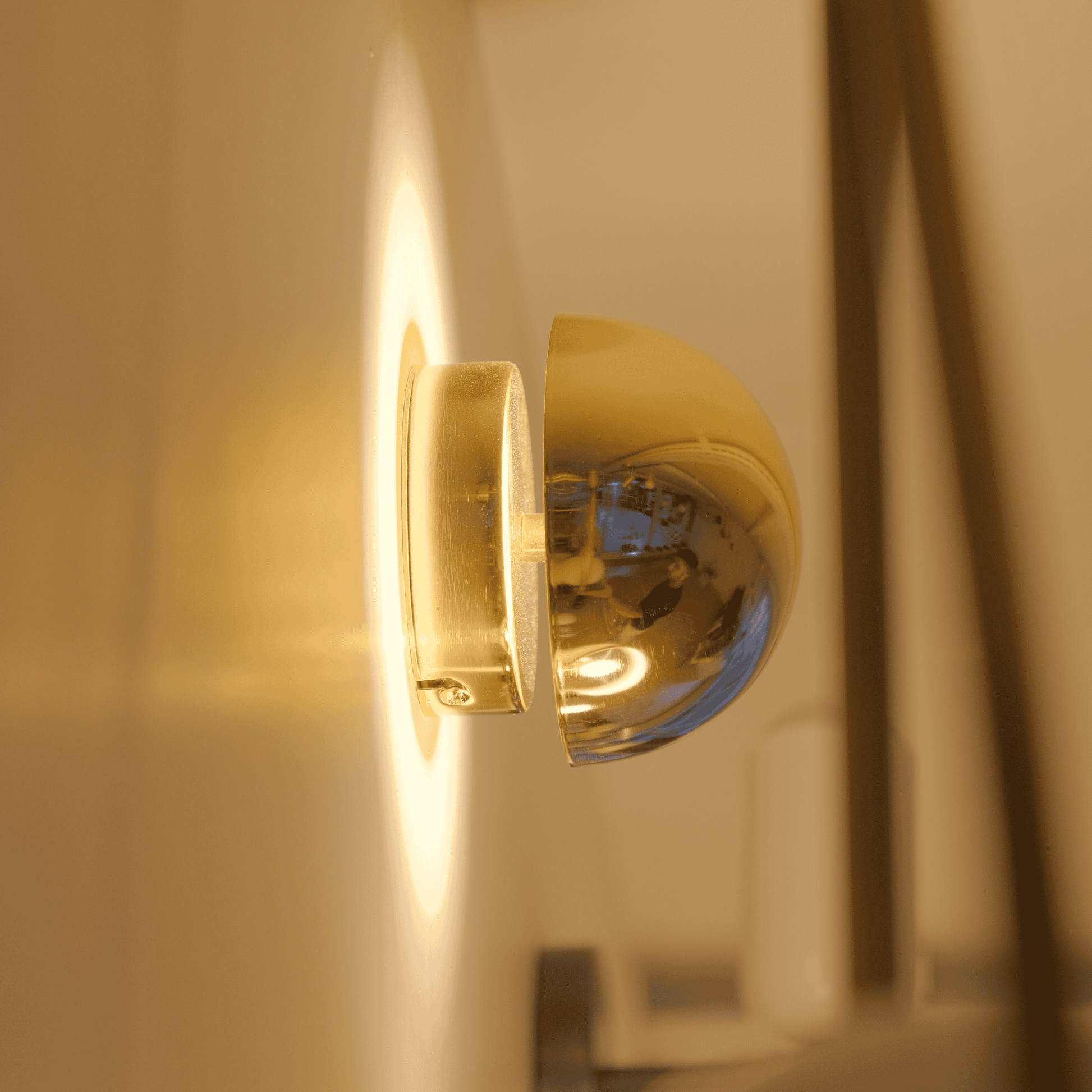 A brass dome wall sconce mounted on a wall emits soft white ambient light.
