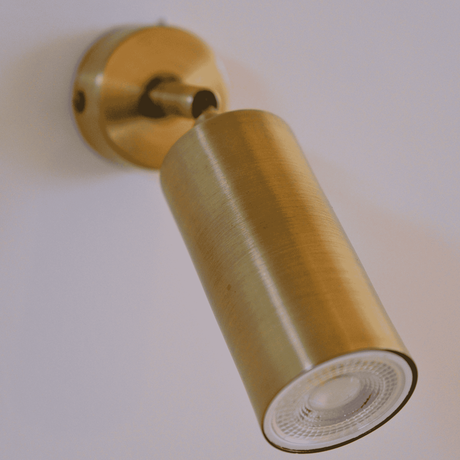 Wall-mounted brass cylinder sconce illuminating a neutral wall with soft warm light.