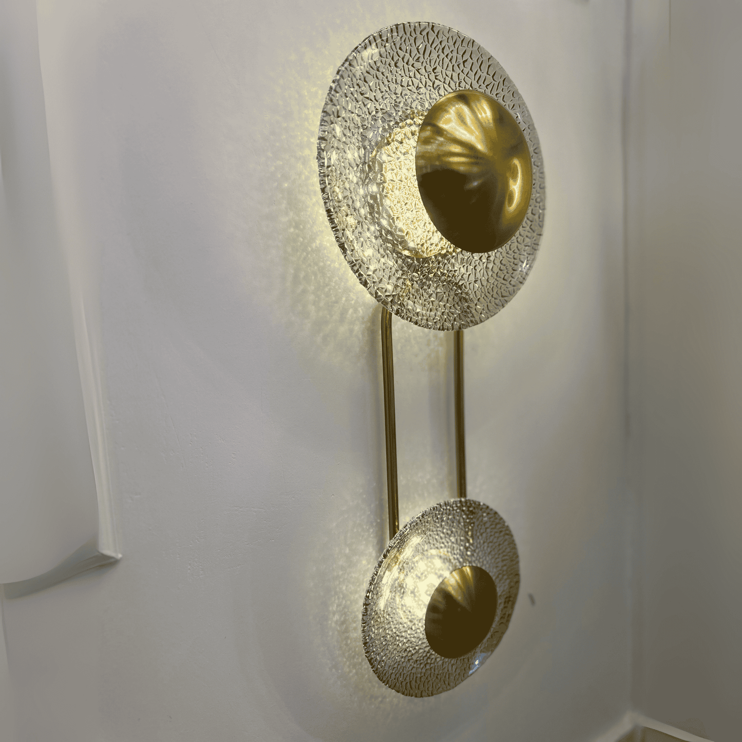 Side angle of modern brass and glass double-disc wall sconce on white wall.