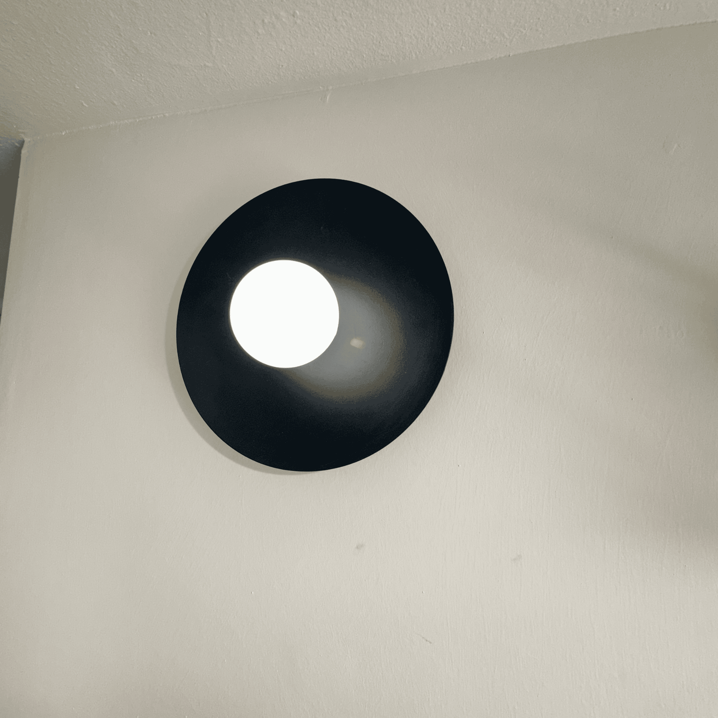 Black disc wall sconce with bright center glow for bold minimalist interior lighting.
