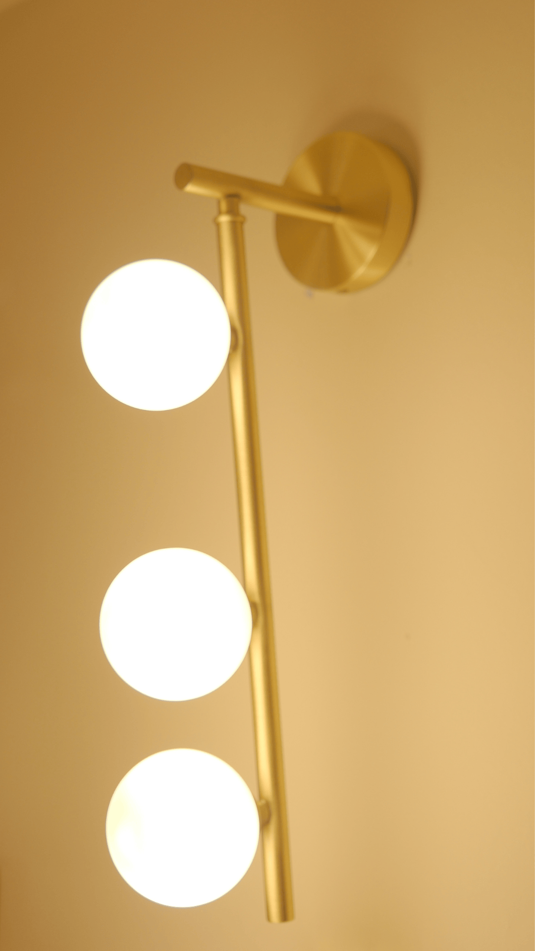 Side-angle view of glowing brass wall sconce with three frosted glass globes.