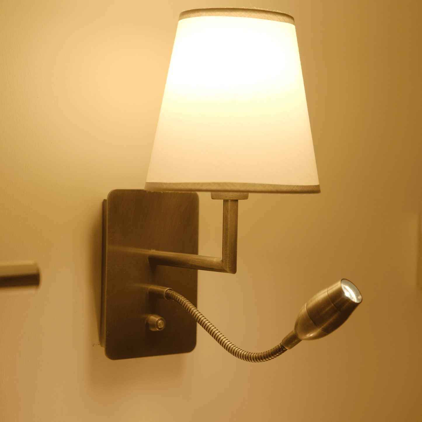 Wall sconce emitting warm light with fabric shade and adjustable metal reading arm.