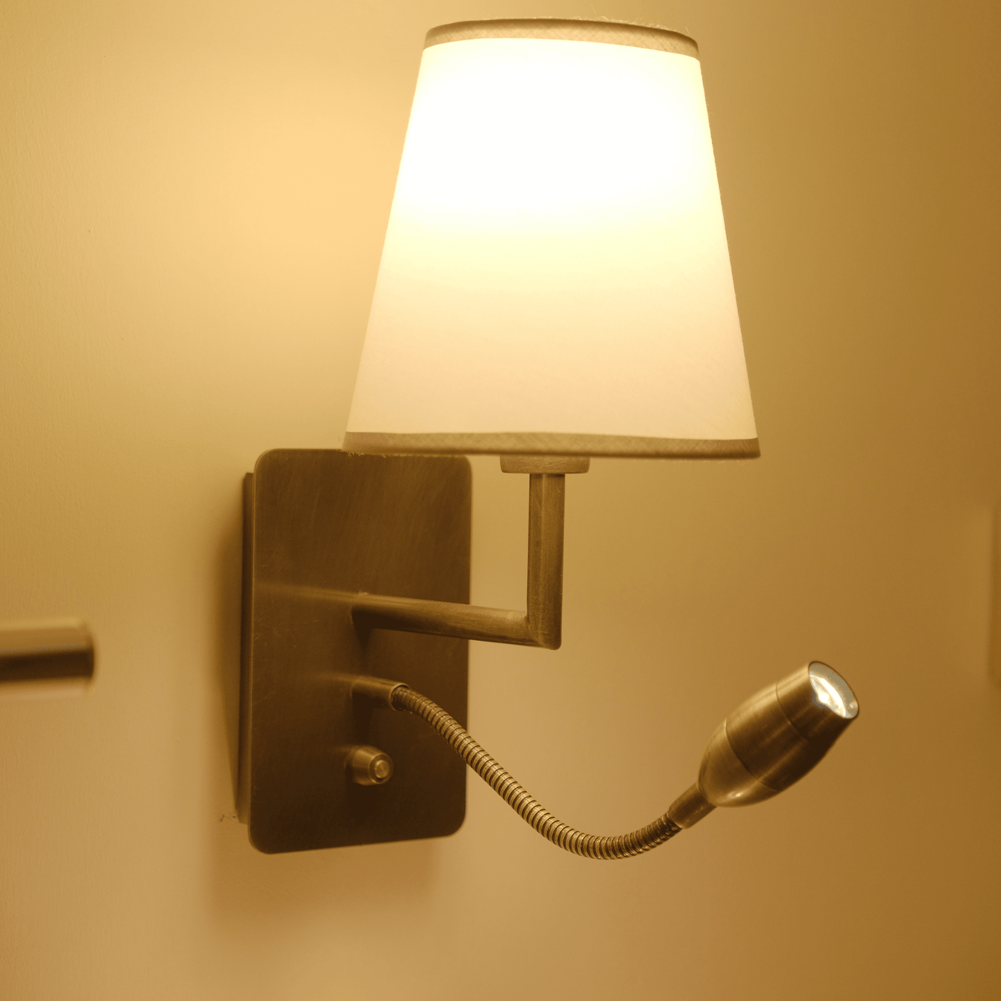 Wall sconce emitting warm light with fabric shade and adjustable metal reading arm.