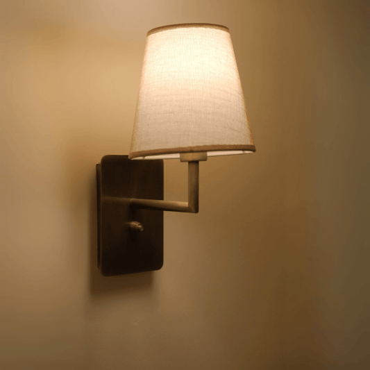 Vintage-style wall sconce with bronze backplate and beige tapered fabric shade emitting warm light.