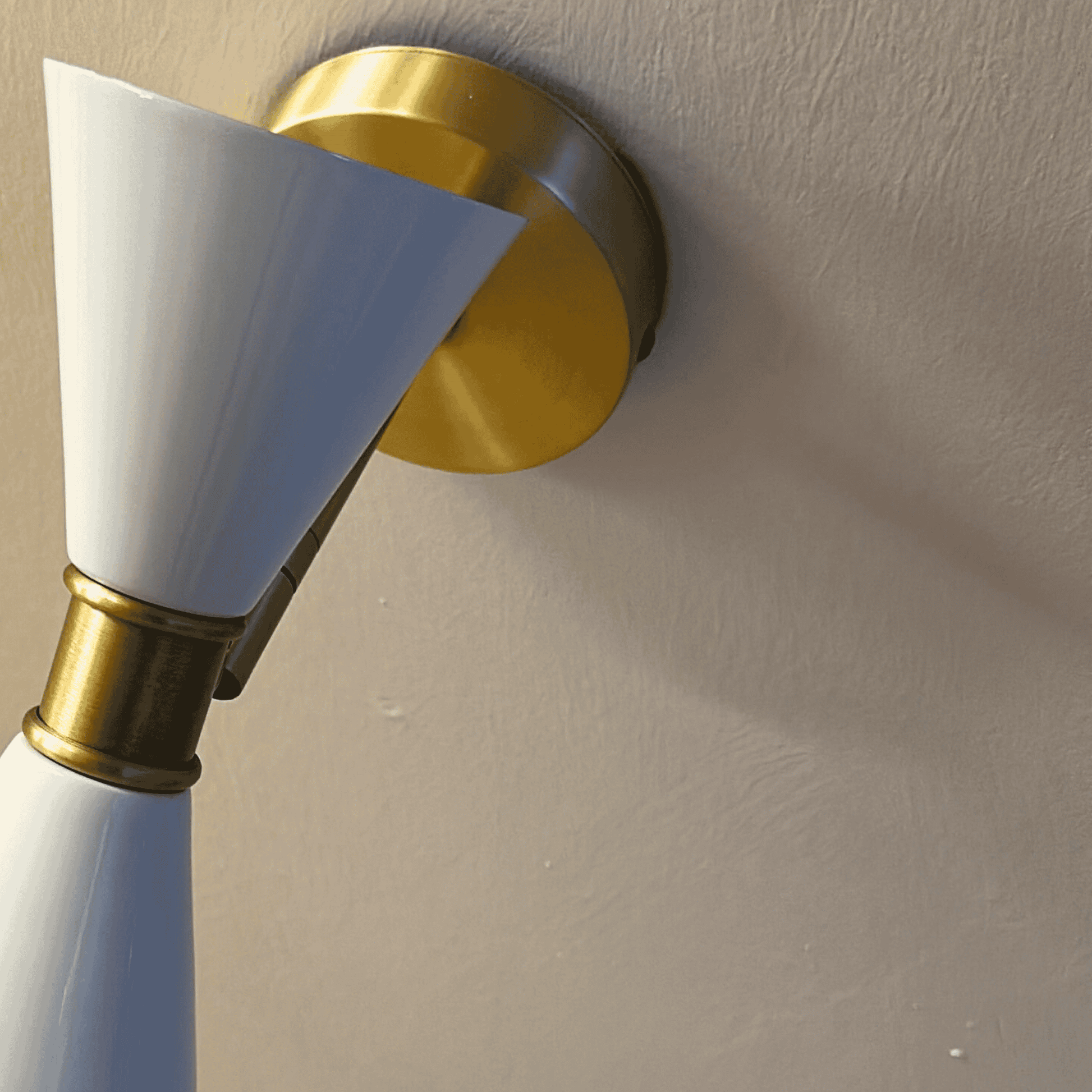 Modern white double-cone wall sconce with brass base emitting ambient up and down lighting.