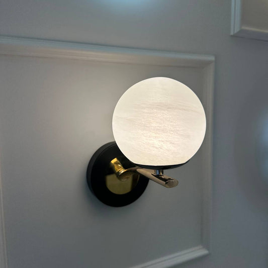 Modern alabaster globe sconce with brass arm and black base on a white wall.
