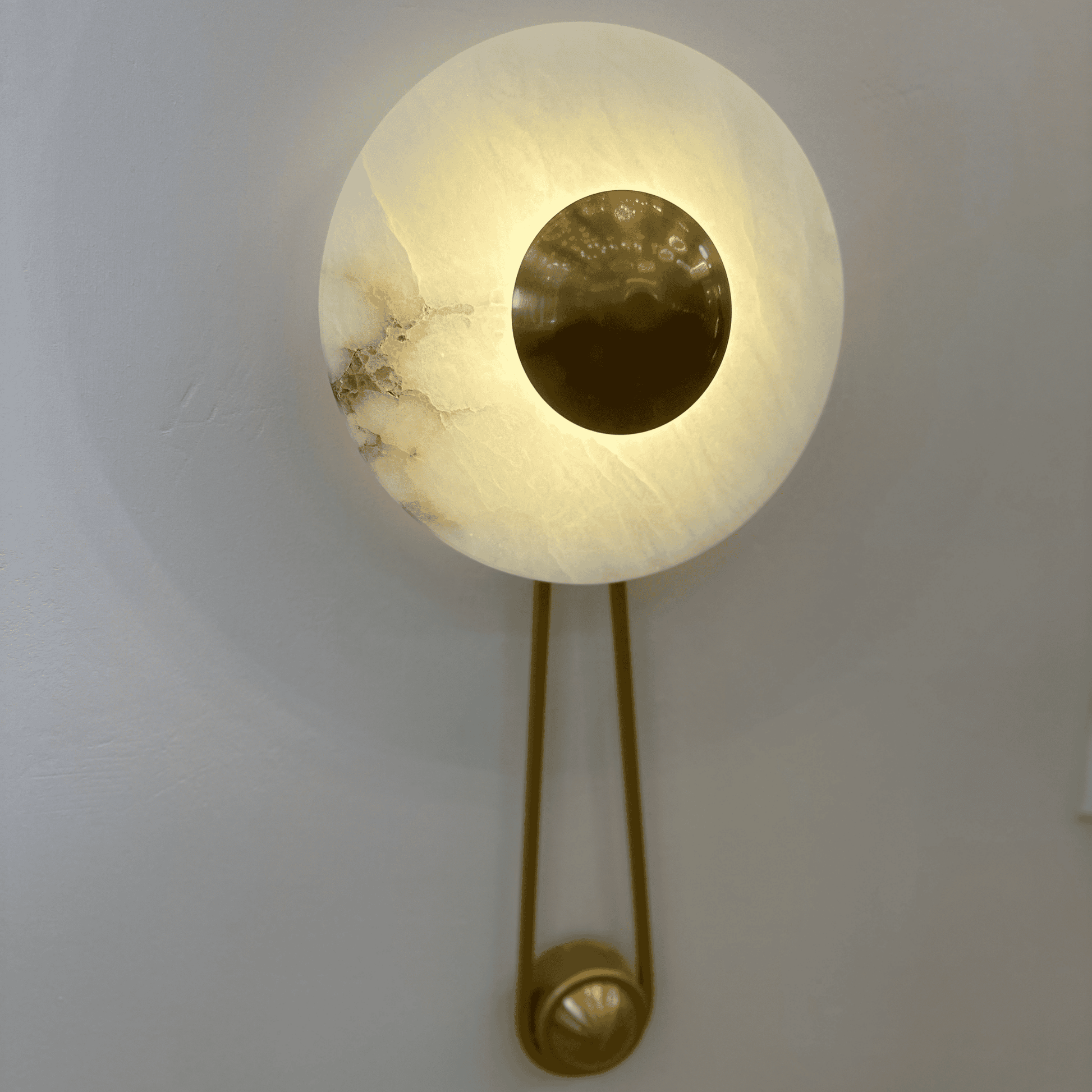 Alabaster wall sconce with brass disc mounted on a neutral-toned wall.