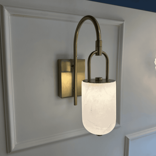 Modern brass and alabaster marble wall sconce with curved arm and soft lighting.