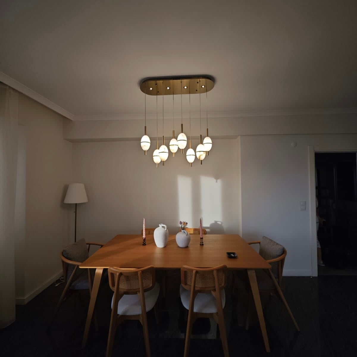 Warm alabaster lighting above a wooden dining table creating subtle shadow play on walls and surfaces.