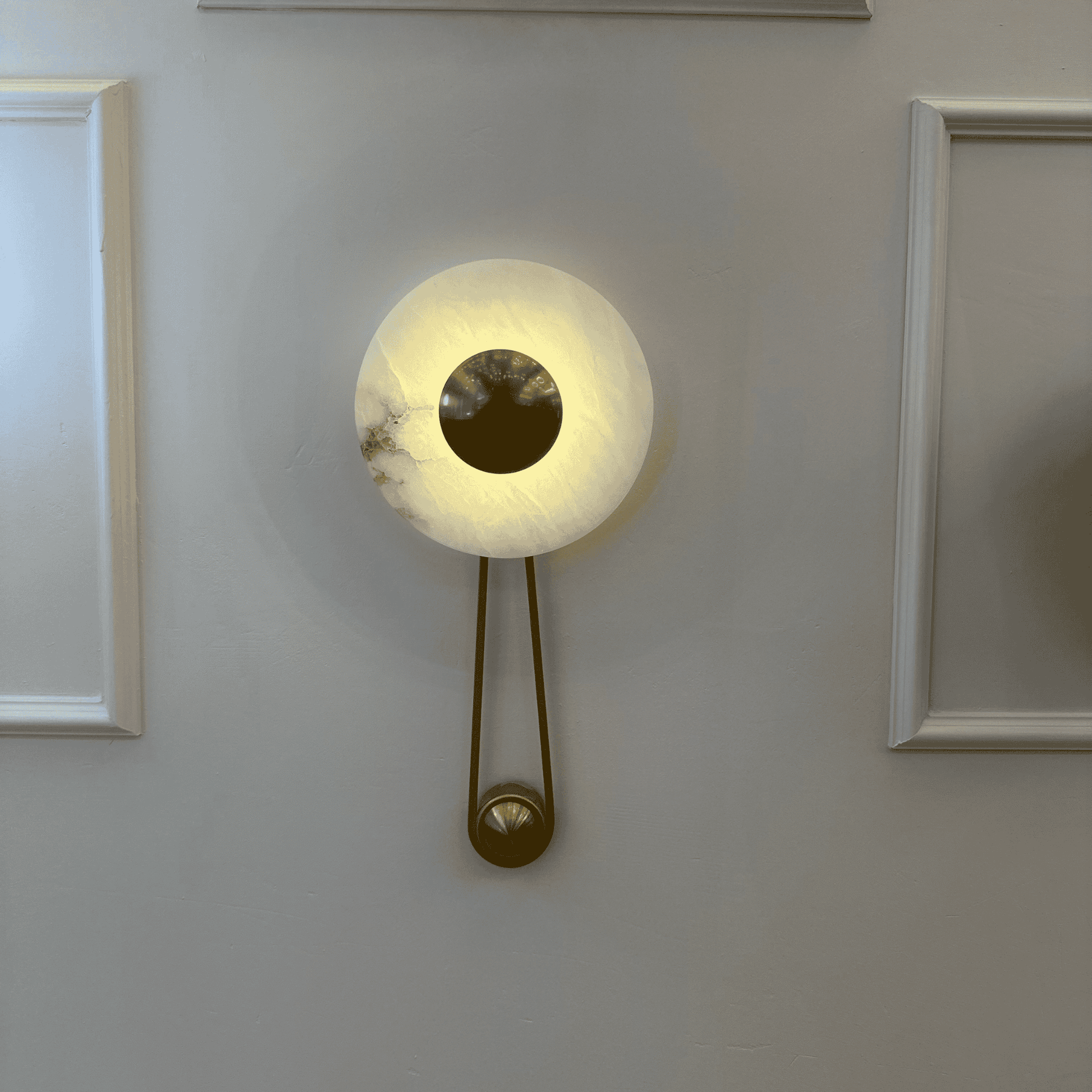 Alabaster wall sconce with a round brass disc and soft backlighting mounted on a paneled wall.