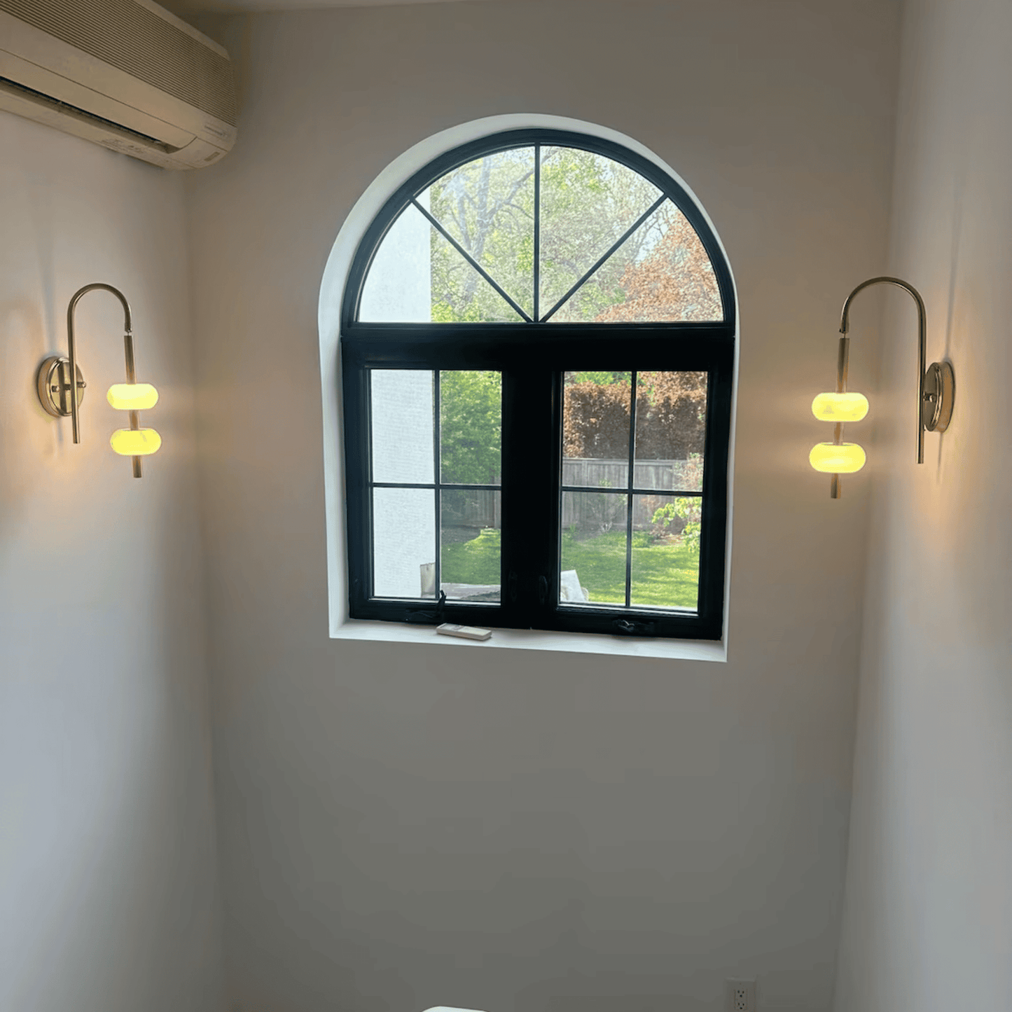 Alabaster and brass wall sconces on each side of a staircase window providing warm light.