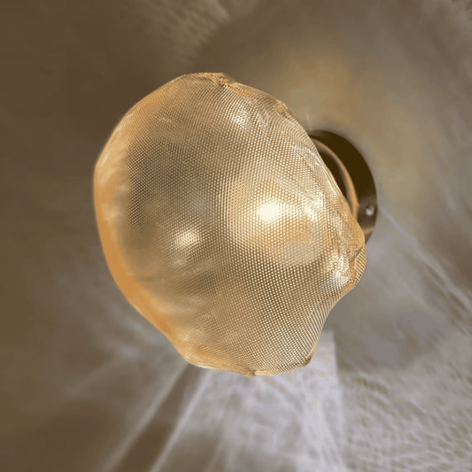 Organic glass wall sconce with natural form and ambient warm light, mounted on bronze.