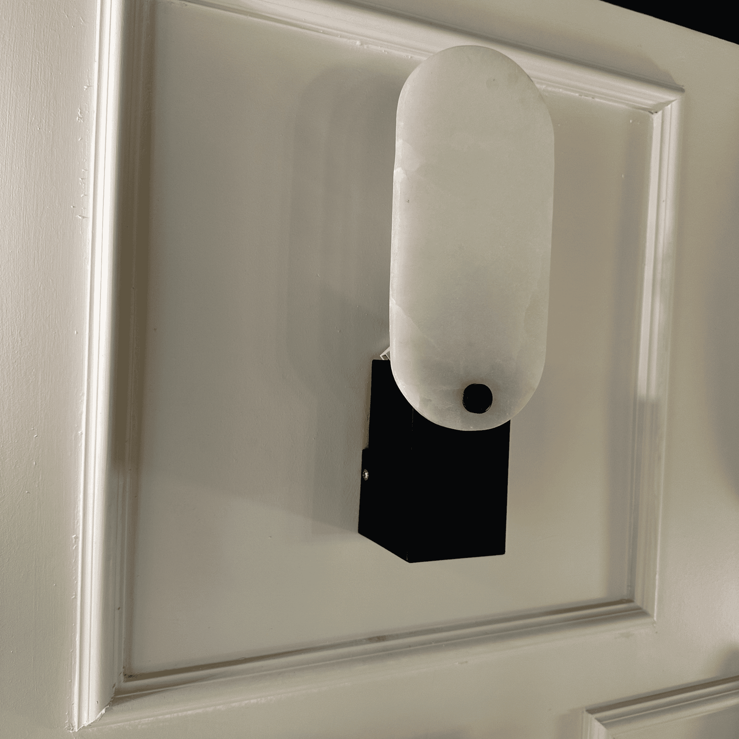 Angled view of matte black square marble wall sconce with rounded white shade.