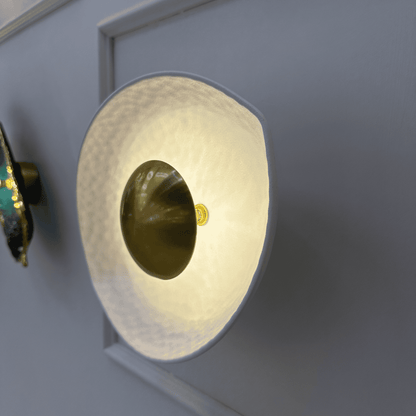 Side view of a deco wall sconce with golden core and softly illuminated hammered white shade.