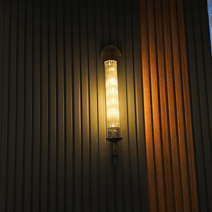 Vertical wall sconce with ribbed glass and warm brass finish mounted on dark fluted wall