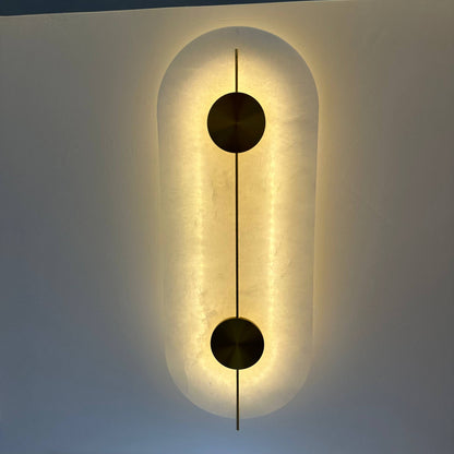 Alabaster wall fixture with brass circular elements, emitting warm indirect lighting in Art Deco style.