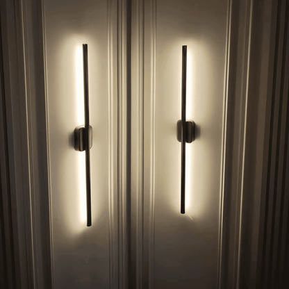 Close-up of two black vertical wall sconces with warm up-and-down light on a decorative paneled wall.