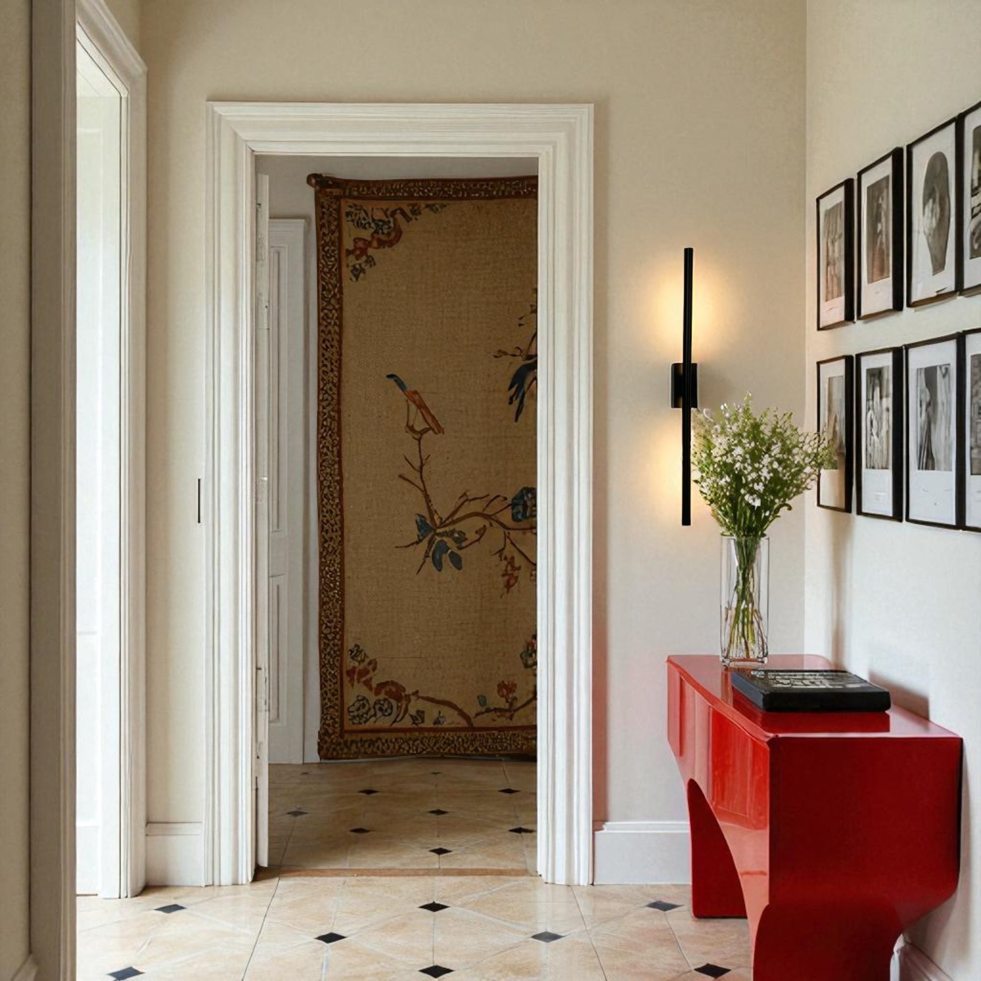 Slim black wall sconce illuminating a hallway with a red console table, floral decor, and traditional tapestry in a modern-classic interior.