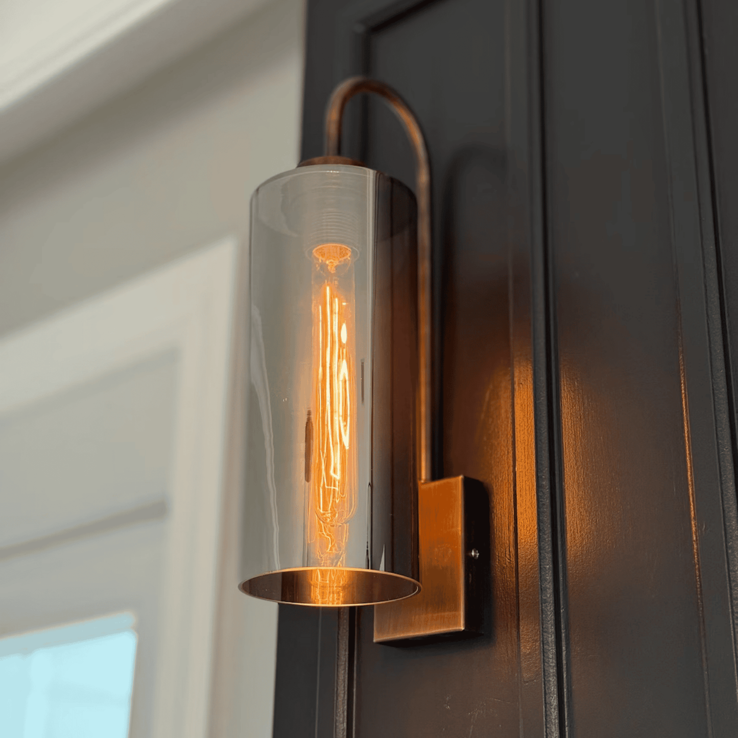 Blown glass wall sconce with Edison bulb and antique finish mounted on a dark paneled wall.