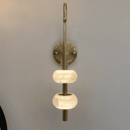Wall-mounted brass sconce with dual alabaster diffusers in a minimalist lighting design.