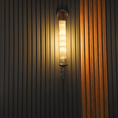 Antique brass wall sconce with fluted glass, mounted on a textured wood panel wall