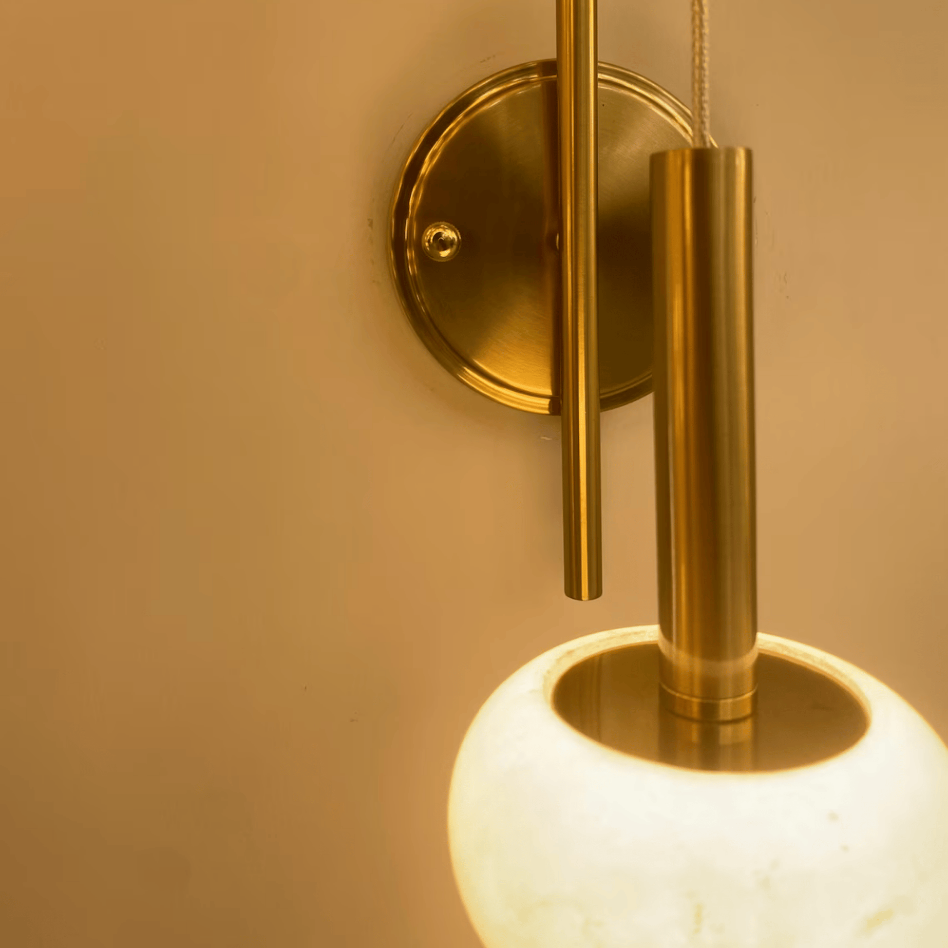 Macro image of modern alabaster wall sconce with brushed brass mount and glowing shade.