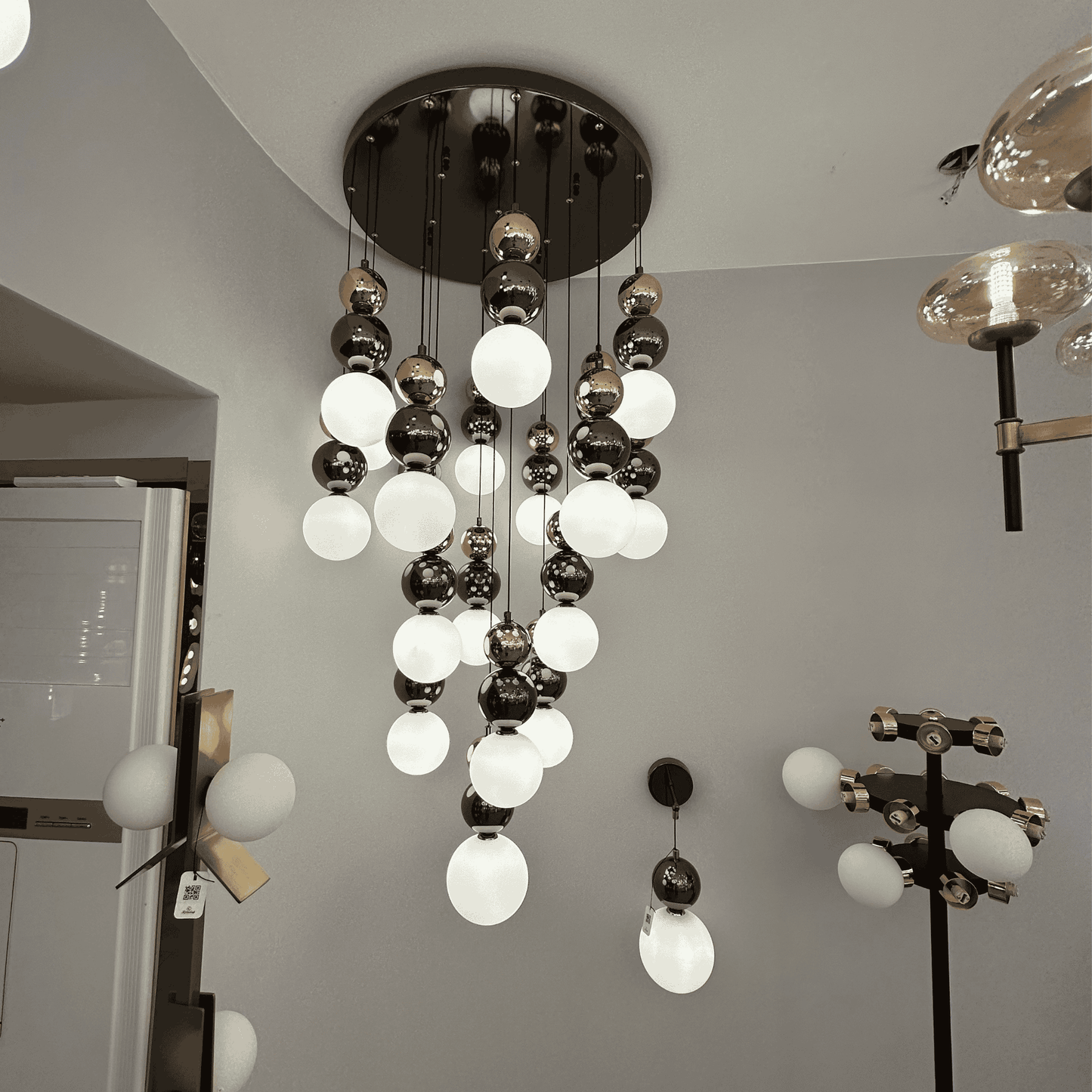 A modern pendant light featuring milk glass and metallic globes cascading from the ceiling, suited for stairwells or entry spaces.