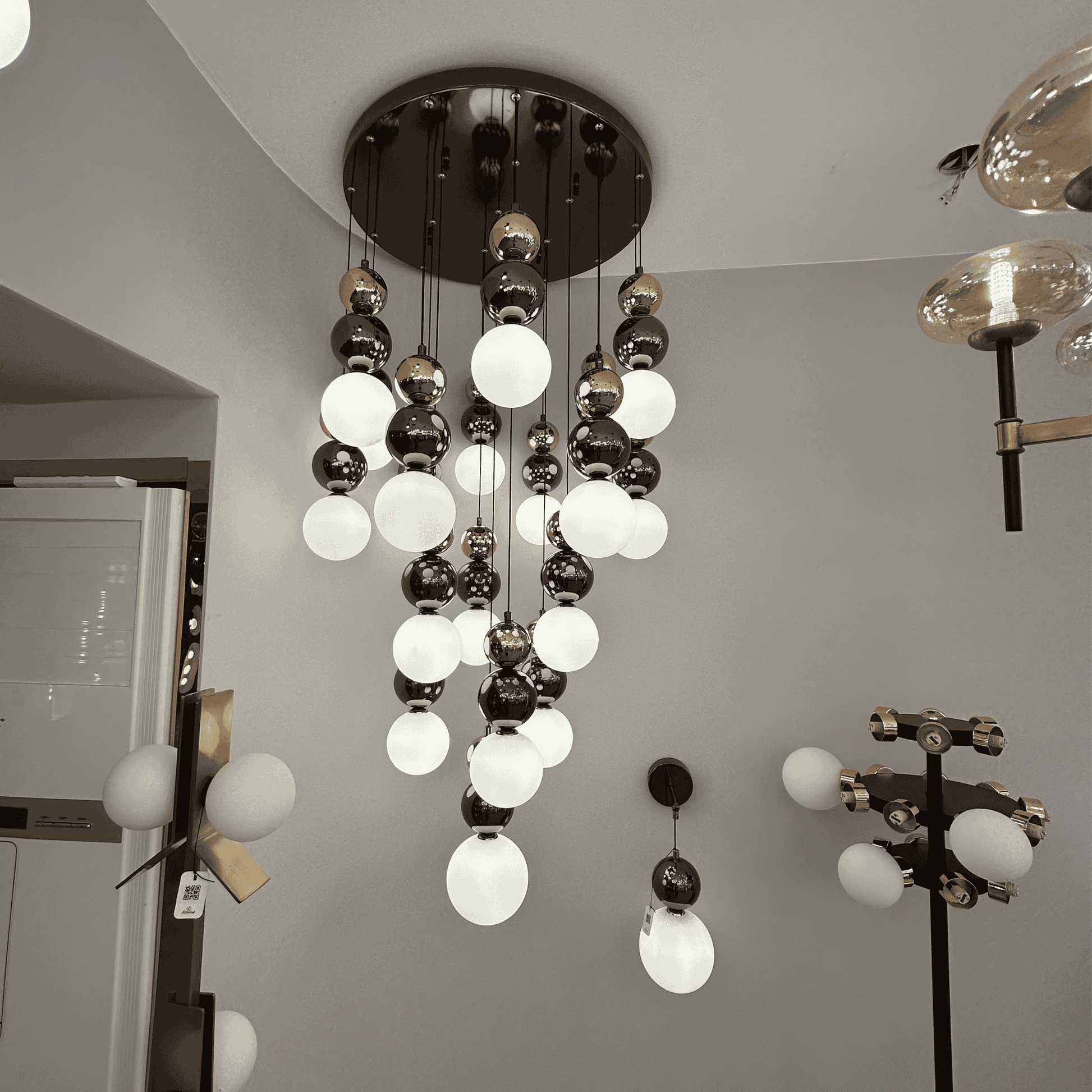 A modern pendant light featuring milk glass and metallic globes cascading from the ceiling, suited for stairwells or entry spaces.