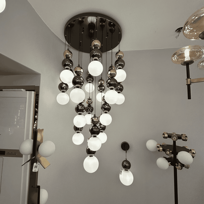 A modern pendant light featuring milk glass and metallic globes cascading from the ceiling, suited for stairwells or entry spaces.