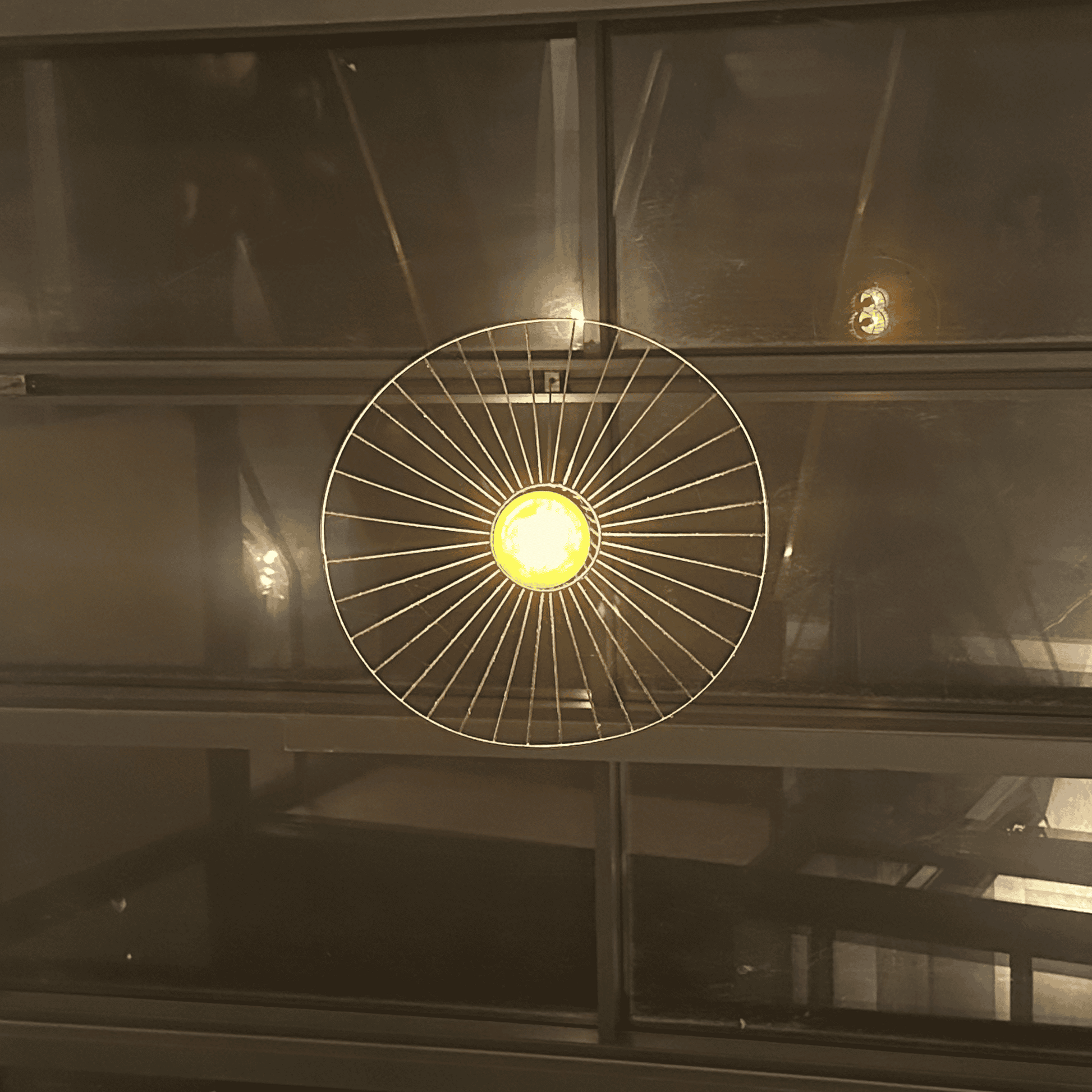 Straw hat pendant light glowing centrally against dark glass panels in an industrial interior.